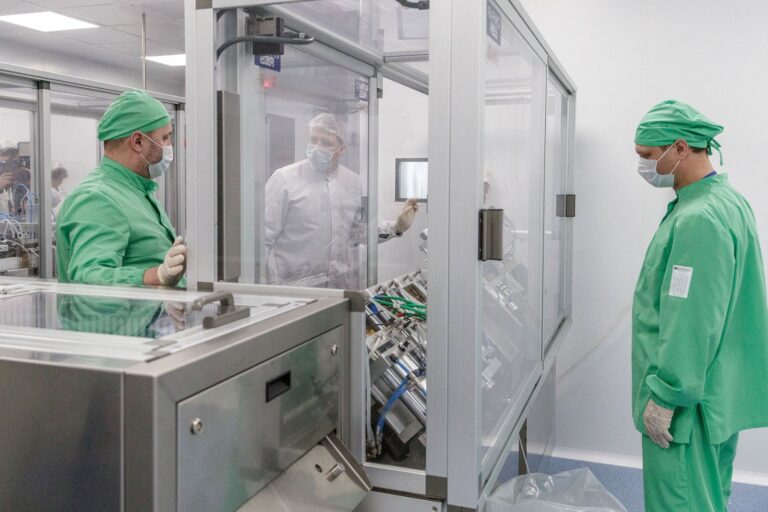 Cleanroom pharmaceutical manufacturing technicians operating precision equipment in a sterile production facility