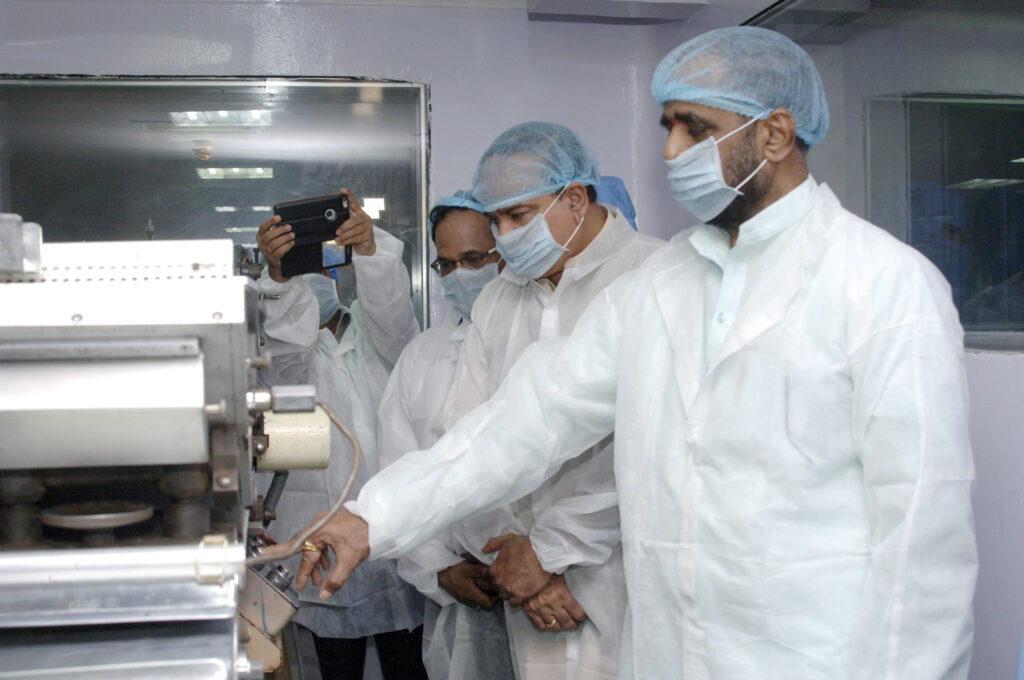 Pharmaceutical manufacturing technicians in cleanroom gowns inspecting tablet production equipment