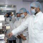 Pharmaceutical manufacturing technicians in cleanroom gowns inspecting tablet production equipment