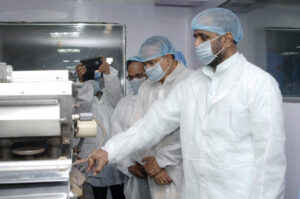 Pharmaceutical manufacturing technicians in cleanroom gowns inspecting tablet production equipment