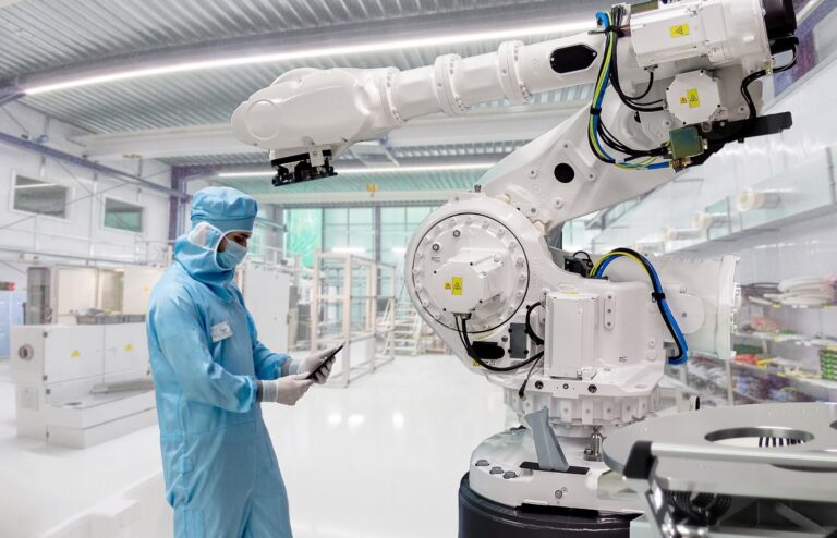 Field service engineer working on an articulated robot inside an ISO 14644-1 Class 6 cleanroom used to manufacture medical device components, illustrating medical device supply chain disruption risk