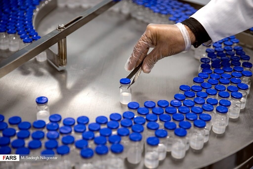 Gloved technician handling vials on a pharmaceutical vaccine production line, representing API and drug supply chains exposed to tariff risk