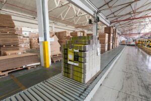 Palletised corrugated shipping boxes on a roller conveyor in a consumer goods packaging warehouse, illustrating AI supply chain risk management for packaging suppliers