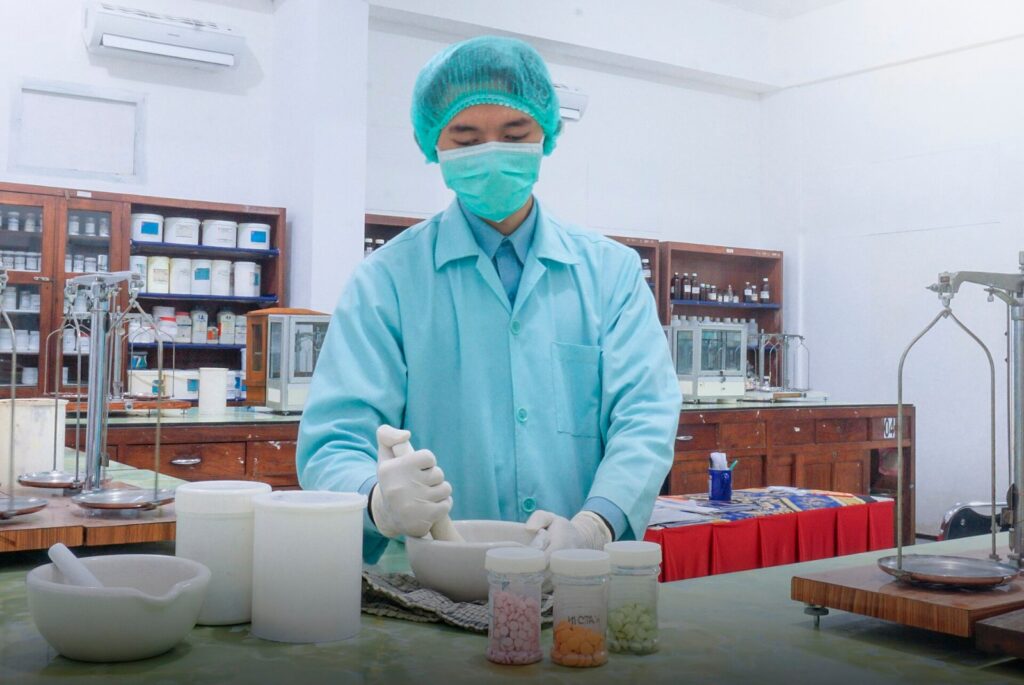 Pharmaceutical technician in protective gear weighing ingredients in a lab, illustrating pharmaceutical supplier risk monitoring