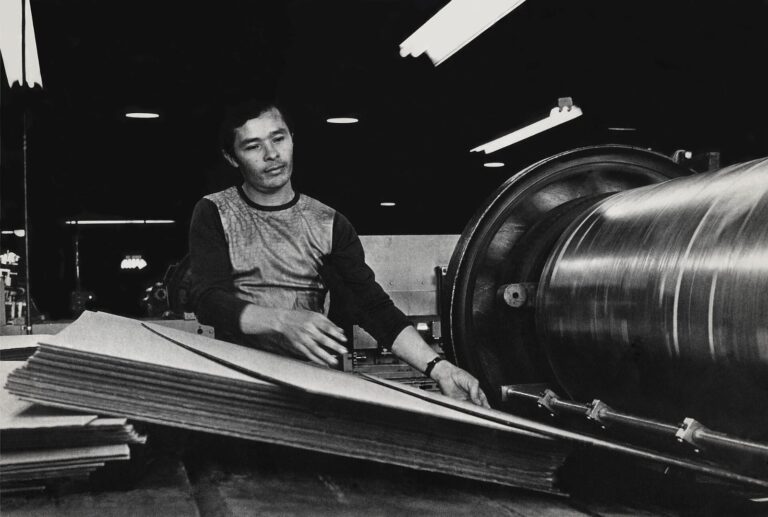 Worker operating a labeling machine on cardboard boxes at a consumer goods packaging factory, illustrating packaging supplier risk