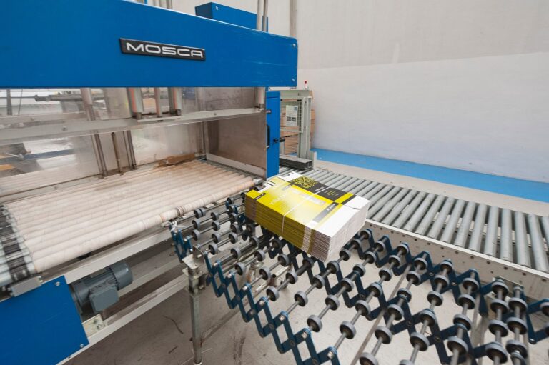 Strapped corrugated shipping boxes on a conveyor in a consumer goods packaging line, illustrating supply chain disruption financial impact