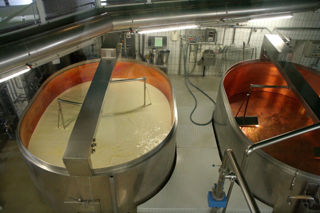 Stainless steel cheese vats separating curds and whey in a dairy plant, illustrating sub-tier supplier risk management in food and beverage